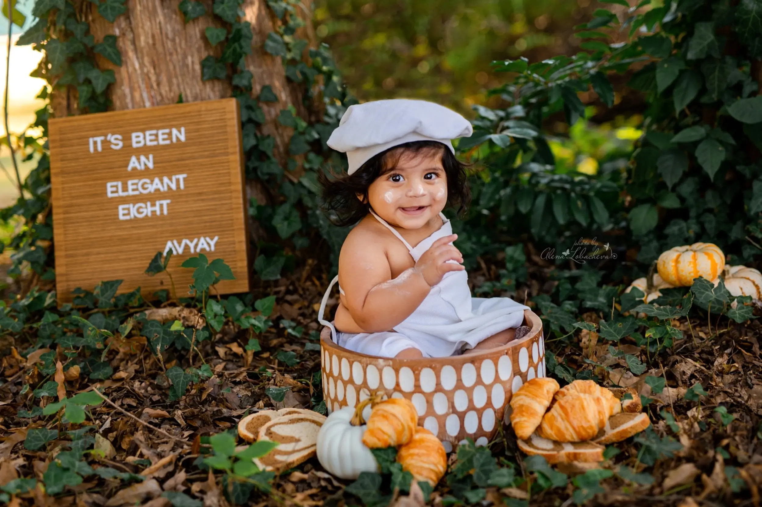 Smiling baby dressed as a baker in an outdoor fall milestone portrait