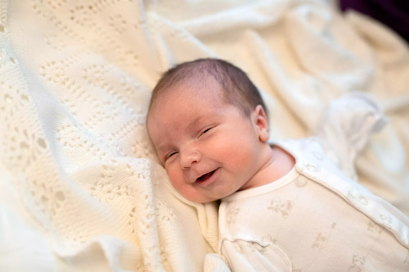 Smiling newborn baby wrapped in a cream hospital blanket