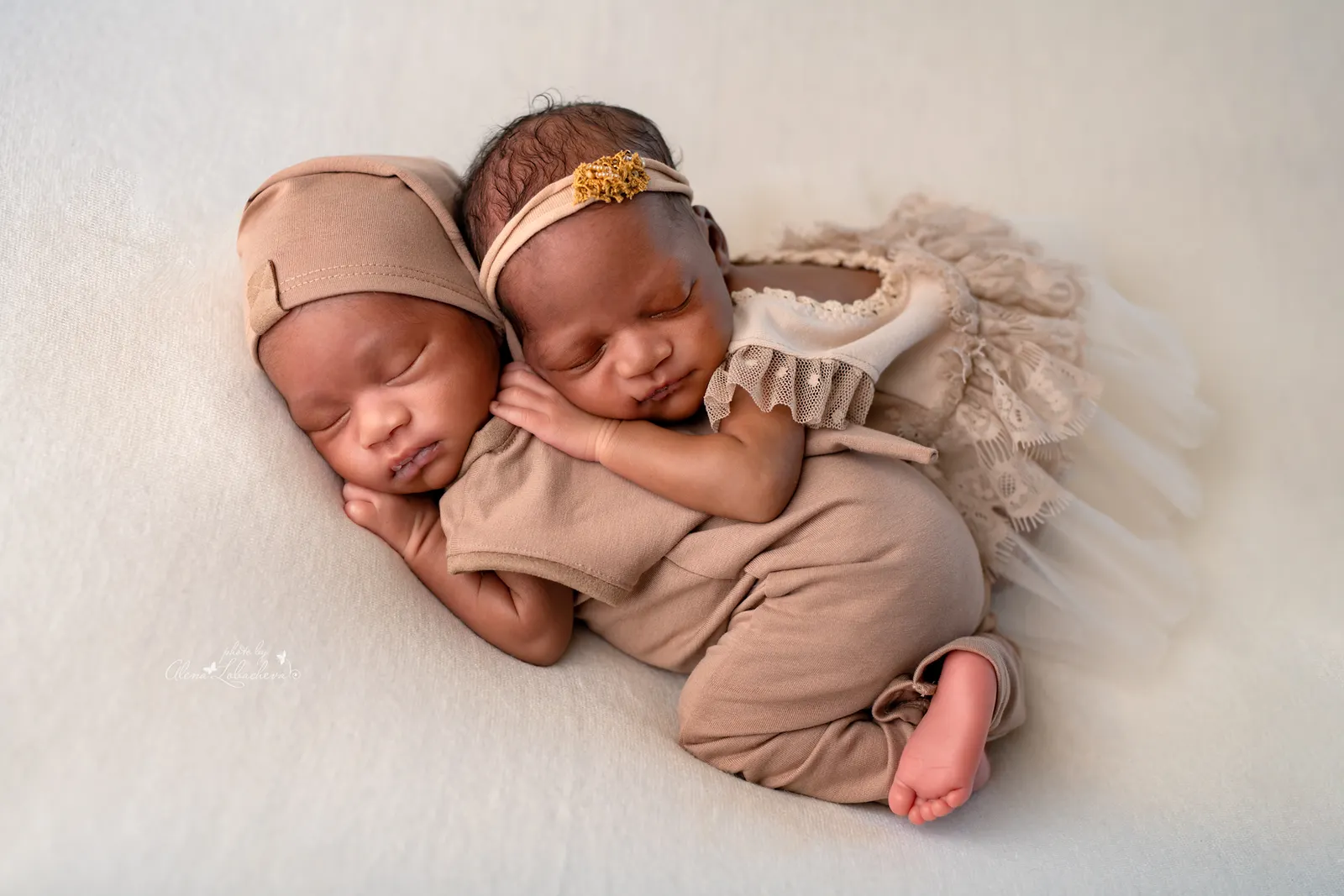 Newborn twins sleeping closely together in matching neutral outfits