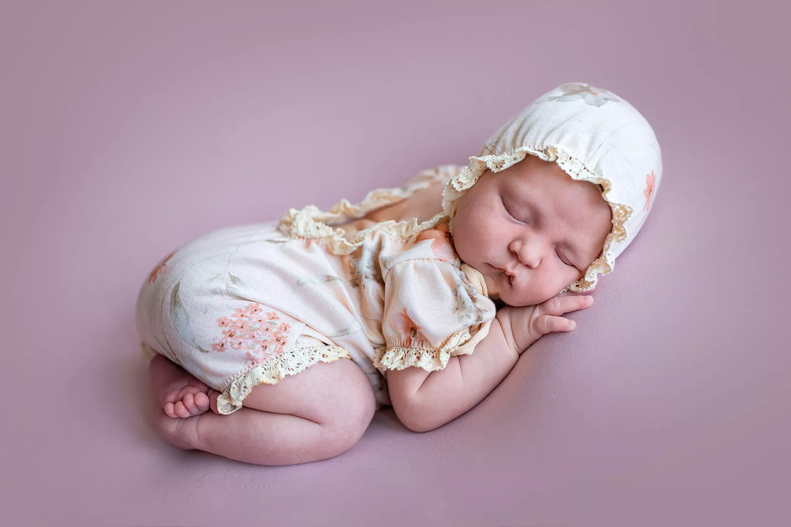 Sleeping newborn baby girl in a floral romper and white bonnet